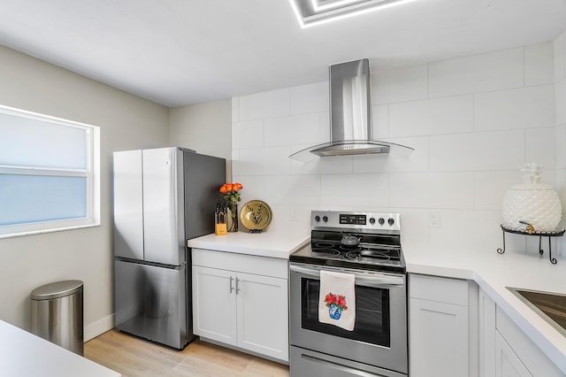 kitchen with appliances with stainless steel finishes, white cabinetry, wall chimney range hood, and light hardwood / wood-style floors