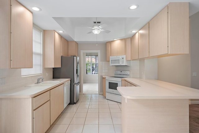 kitchen featuring kitchen peninsula, light brown cabinetry, sink, and white appliances