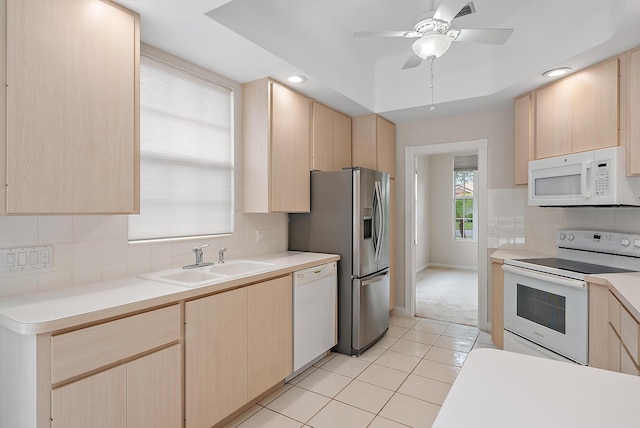 kitchen with light brown cabinets, a tray ceiling, sink, and white appliances