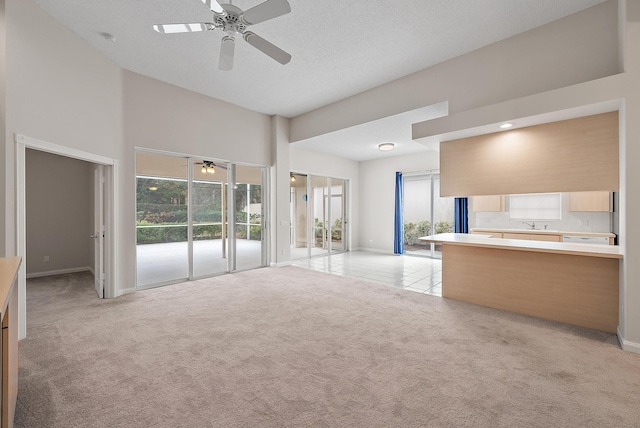 unfurnished living room with ceiling fan, plenty of natural light, a high ceiling, and light carpet