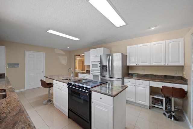 kitchen featuring white cabinetry, light tile patterned flooring, white appliances, and a kitchen island with sink