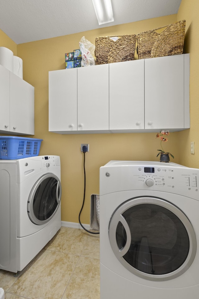 washroom featuring washing machine and clothes dryer, light tile patterned floors, and cabinets