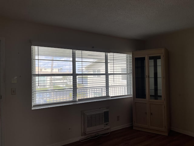 empty room with a wall mounted AC, dark hardwood / wood-style flooring, and a textured ceiling