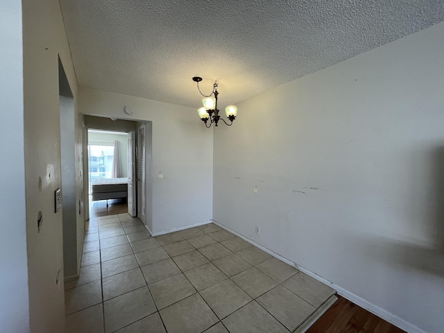 tiled empty room featuring a notable chandelier and a textured ceiling