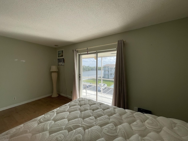 bedroom with a water view, access to exterior, a textured ceiling, and hardwood / wood-style floors