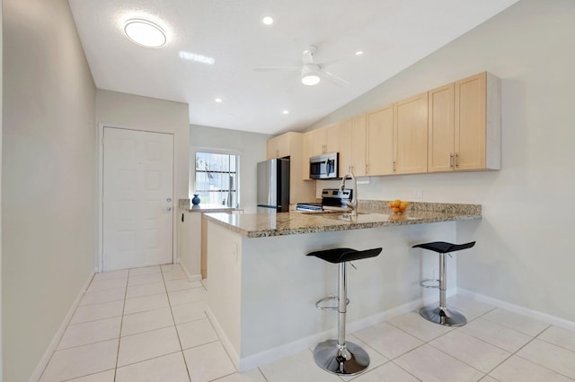 kitchen with light brown cabinets, light tile patterned floors, appliances with stainless steel finishes, light stone counters, and kitchen peninsula