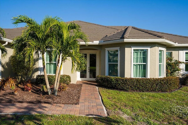 view of front of property featuring stucco siding, a tile roof, a front lawn, and french doors