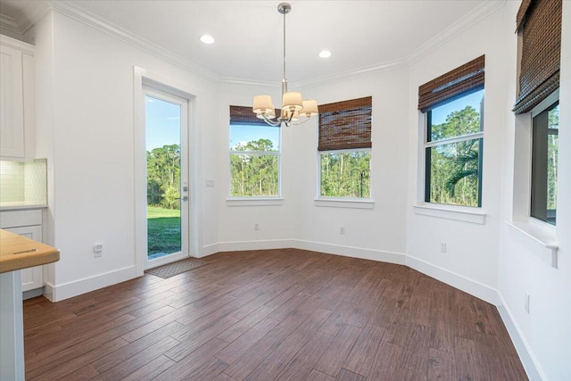 unfurnished dining area with dark wood-type flooring, ornamental molding, a chandelier, and a wealth of natural light