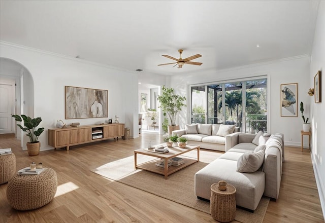 living room with arched walkways, light wood-style flooring, ornamental molding, ceiling fan, and baseboards