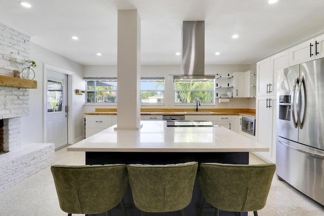 kitchen featuring island exhaust hood, appliances with stainless steel finishes, a kitchen bar, white cabinets, and sink