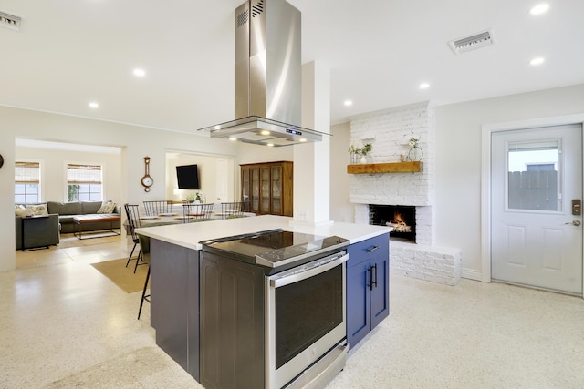 kitchen featuring island exhaust hood, a breakfast bar area, stainless steel electric range, a fireplace, and blue cabinets