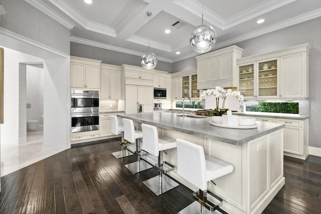 kitchen featuring beamed ceiling, an island with sink, a breakfast bar area, decorative backsplash, and built in appliances