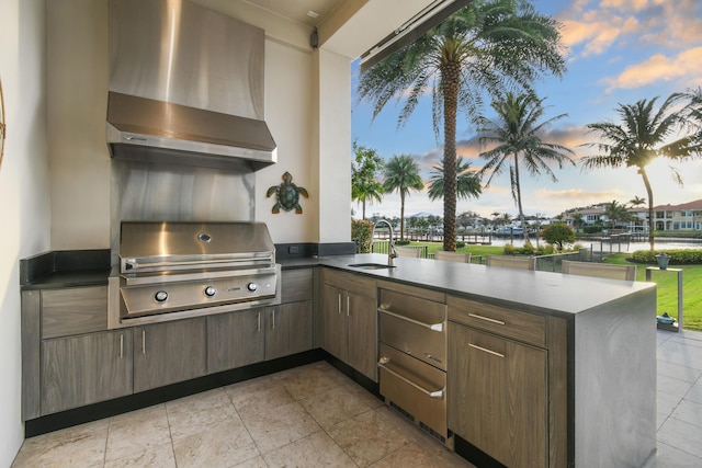 kitchen with wall chimney exhaust hood, sink, a water view, dark brown cabinets, and kitchen peninsula