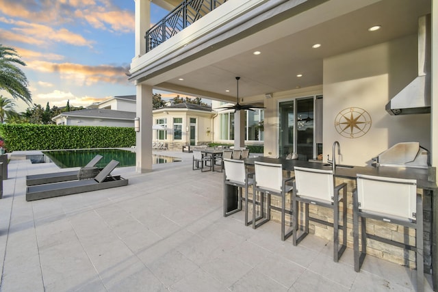 patio terrace at dusk with a balcony, an outdoor kitchen, and an outdoor wet bar