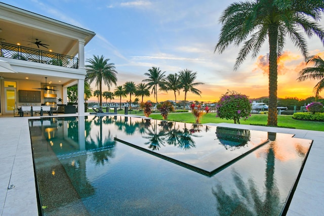 pool at dusk with a patio and ceiling fan