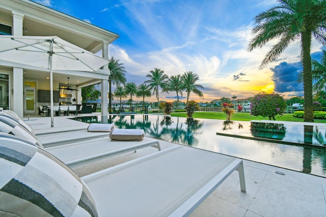 pool at dusk featuring ceiling fan and a patio