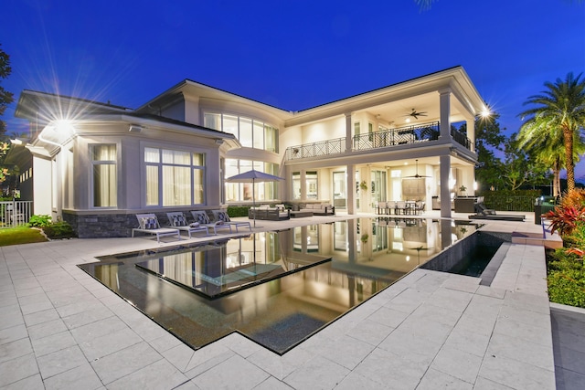 13791 Baycliff Dr, Juno Beach, FL 33408 - back of house at twilight with a balcony, a patio area, a ceiling fan, and an infinity pool