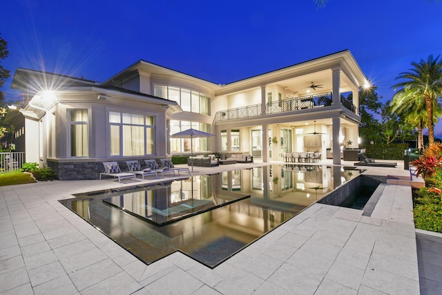 back house at twilight with ceiling fan, a balcony, an outdoor living space, and a patio area