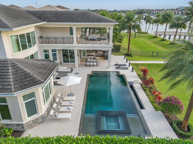 back of house with a patio area, a water view, a balcony, a yard, and a swimming pool with hot tub