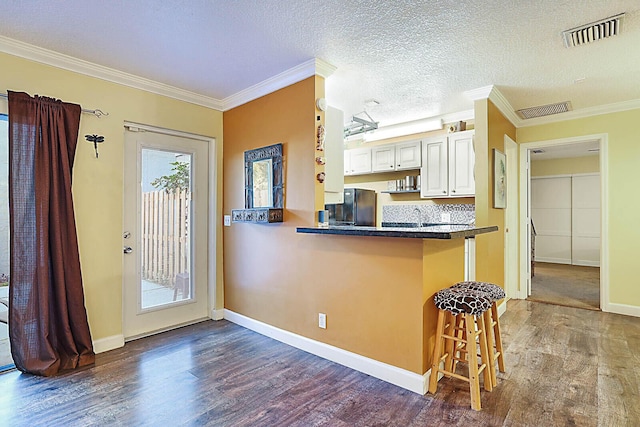 kitchen with a breakfast bar, white cabinets, crown molding, fridge, and kitchen peninsula