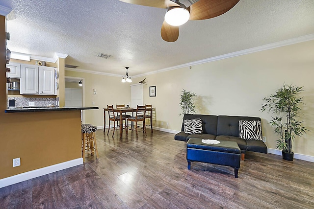 living room featuring ceiling fan with notable chandelier, dark hardwood / wood-style flooring, a textured ceiling, and crown molding