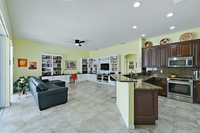 kitchen featuring tasteful backsplash, kitchen peninsula, stove, dark stone counters, and a breakfast bar