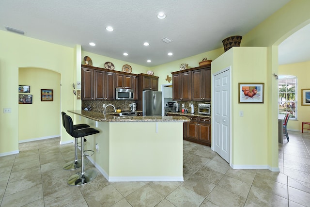 kitchen featuring stainless steel appliances, tasteful backsplash, a breakfast bar area, and stone countertops