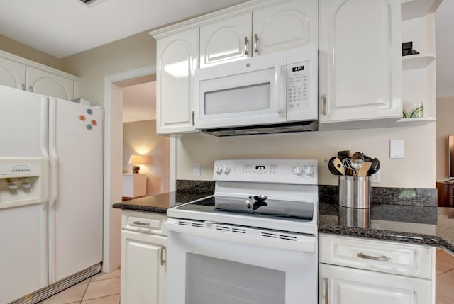 kitchen with white appliances, white cabinetry, dark stone counters, and light tile patterned floors