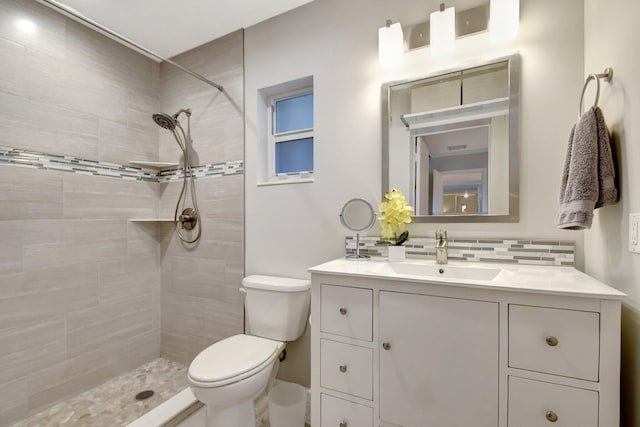 bathroom with a tile shower, backsplash, vanity, and toilet