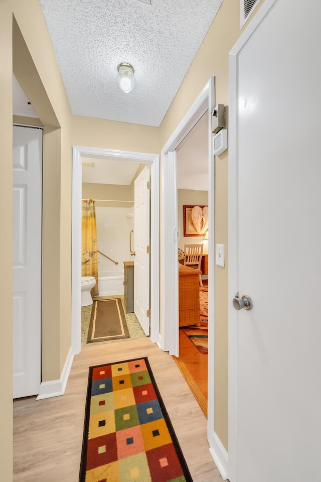 corridor with a textured ceiling and light hardwood / wood-style flooring