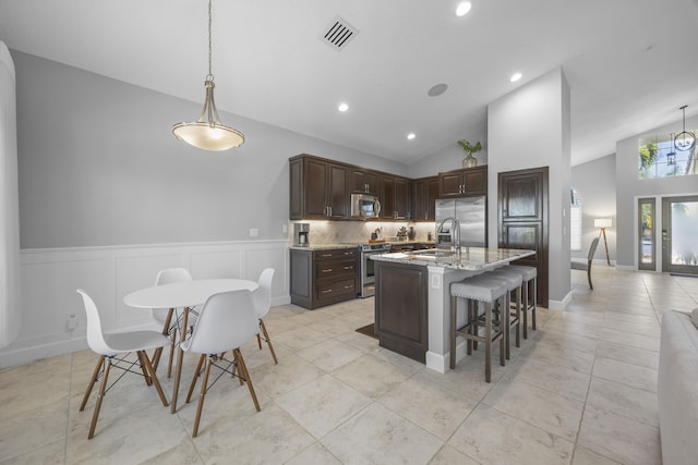 kitchen featuring light stone countertops, pendant lighting, dark brown cabinetry, stainless steel appliances, and backsplash