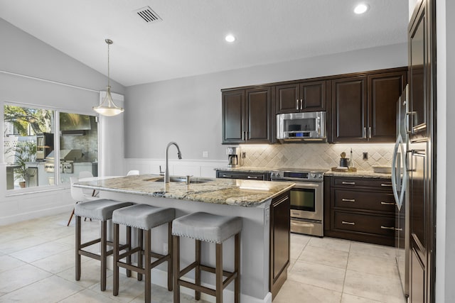 kitchen with stainless steel appliances, sink, vaulted ceiling, light stone counters, and a center island with sink