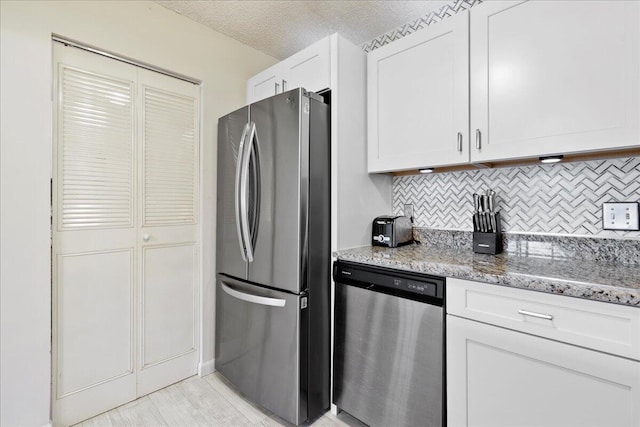 kitchen with backsplash, white cabinets, light stone countertops, a textured ceiling, and stainless steel appliances