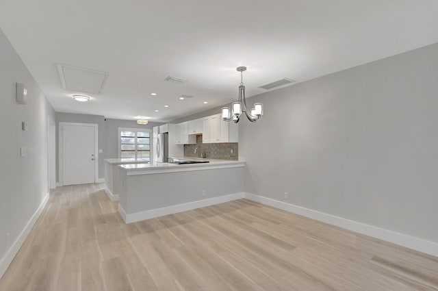 kitchen with kitchen peninsula, hanging light fixtures, tasteful backsplash, light wood-type flooring, and white cabinetry