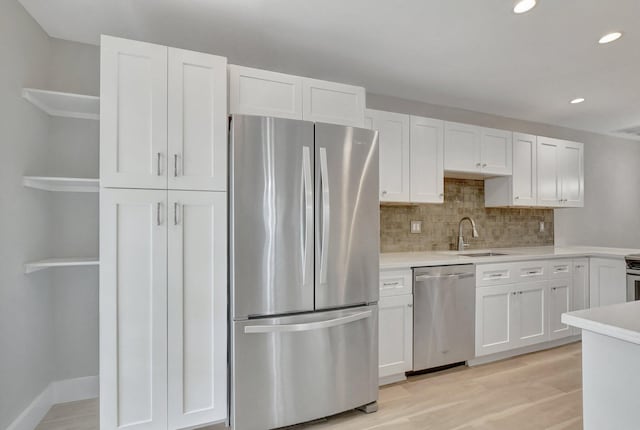 kitchen featuring stainless steel appliances, light wood-type flooring, sink, white cabinetry, and backsplash