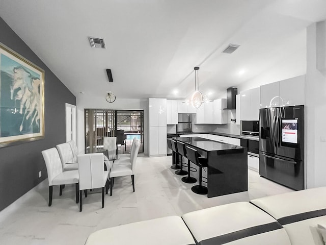 kitchen with pendant lighting, lofted ceiling, wall chimney range hood, stainless steel refrigerator with ice dispenser, and white cabinetry