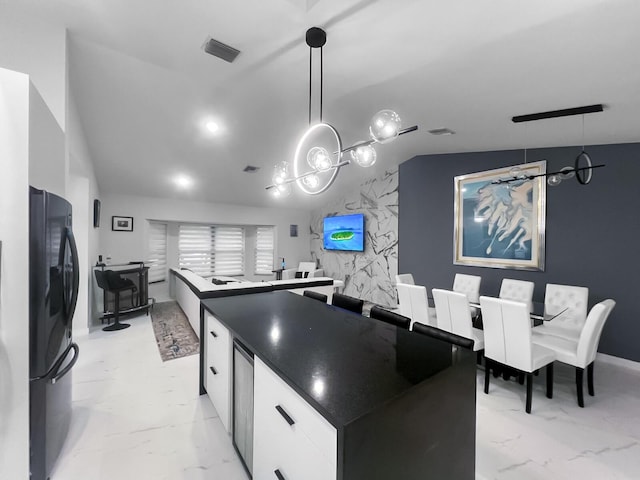 kitchen featuring pendant lighting, black refrigerator, vaulted ceiling, a kitchen island, and white cabinetry