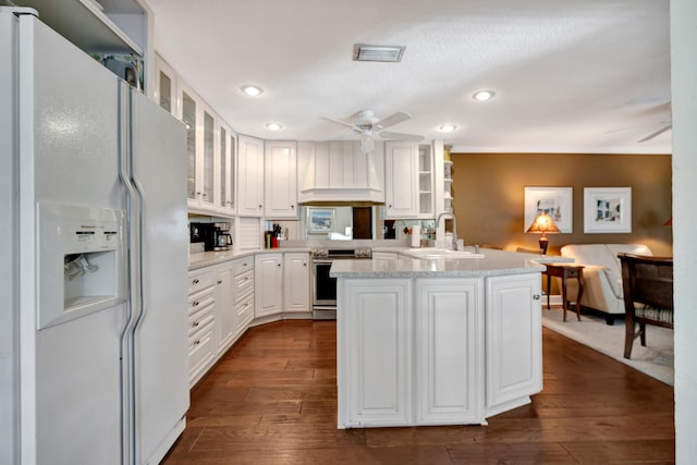 kitchen featuring sink, white refrigerator with ice dispenser, custom range hood, white cabinets, and stainless steel electric range oven