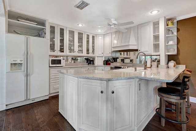 kitchen featuring white appliances, premium range hood, light stone countertops, white cabinets, and kitchen peninsula