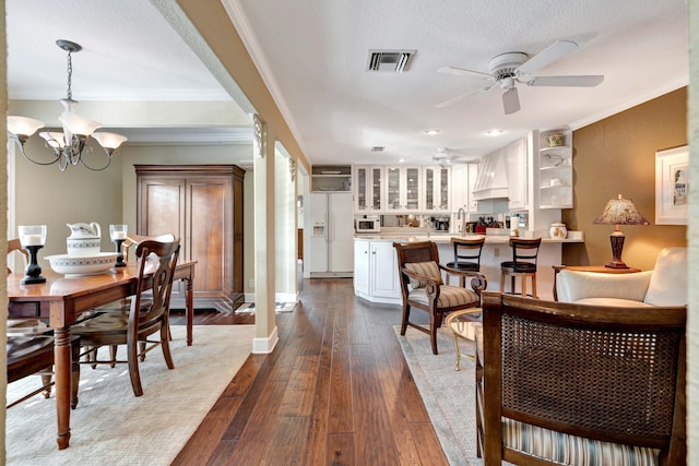 dining room featuring hardwood / wood-style flooring, ornamental molding, ceiling fan with notable chandelier, and a textured ceiling