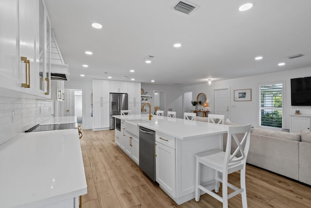 kitchen featuring stainless steel appliances, white cabinetry, and an island with sink