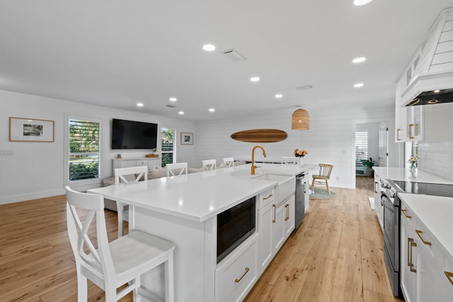 kitchen featuring white cabinetry, a center island with sink, appliances with stainless steel finishes, a kitchen bar, and light hardwood / wood-style flooring