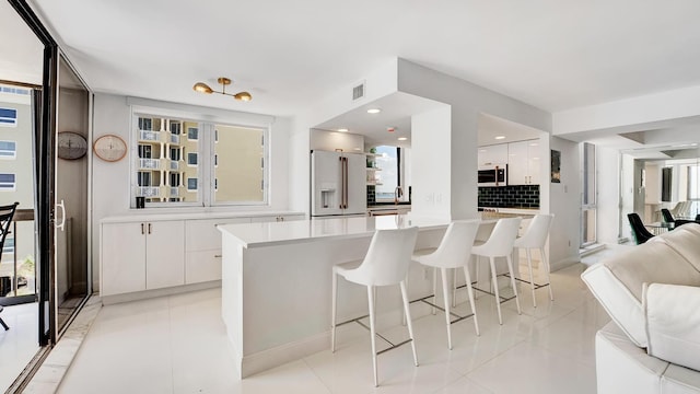 kitchen with white cabinetry, white refrigerator with ice dispenser, backsplash, a breakfast bar area, and light tile patterned flooring