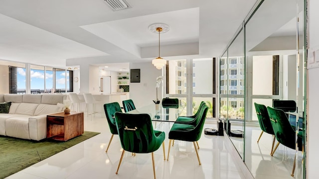 dining area with light tile patterned floors, a raised ceiling, and a wall of windows