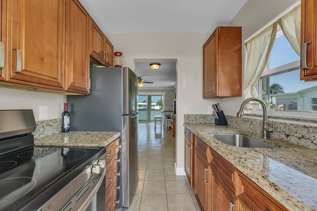 kitchen featuring light stone countertops, light tile patterned floors, stainless steel range with electric stovetop, and sink