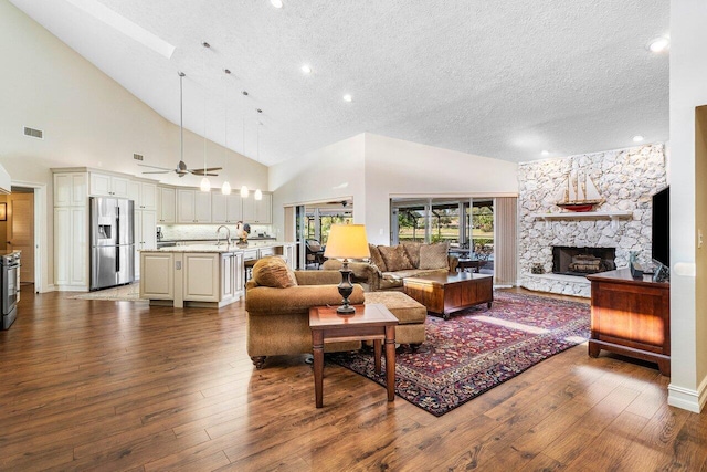 living room with visible vents, high vaulted ceiling, a textured ceiling, dark wood-style floors, and a fireplace