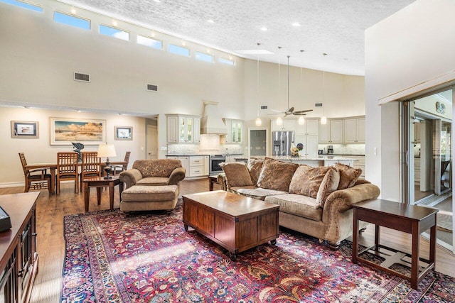 living area with visible vents, a textured ceiling, a high ceiling, and wood finished floors