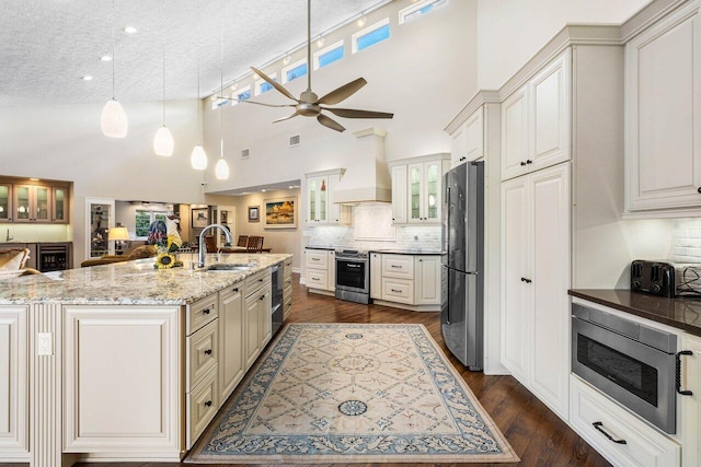 kitchen featuring glass insert cabinets, premium range hood, dark wood-style floors, stainless steel appliances, and a sink