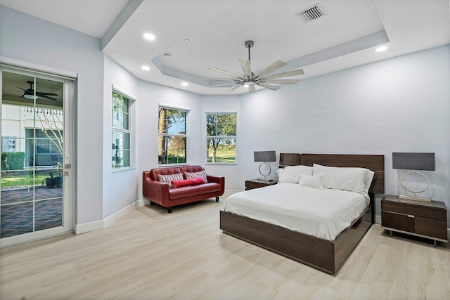 bedroom featuring ceiling fan, access to exterior, light hardwood / wood-style flooring, and a tray ceiling