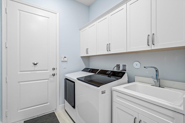 washroom with cabinets, light wood-type flooring, washer and clothes dryer, and sink